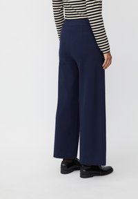 Marineblauwe broek met wijde benen, gemaakt van een gladde stof en voorzien van een elastische tailleband, gecombineerd met zwarte schoenen. Gestreept shirt dat gedeeltelijk zichtbaar is op het bovenlichaam.
