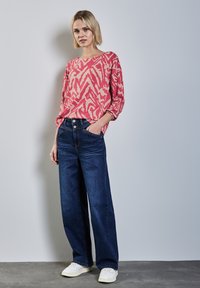 Roze trui met zebramotief, brede donkerblauwe jeans en witte sneakers. De outfit heeft een ontspannen pasvorm en casual ontwerp.