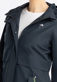 Námořnická vodotěsná bunda s kapucí, s našitým zipem a patentními knoflíky a diskrétním logem deštníku na hrudi. Hladká textura.