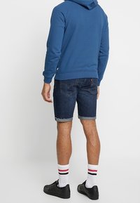 Sininen huppari, jossa on etupuolella kenguru-tasku, yhdistetty tummiin farkkushortseihin, valkoisiin sukkiin, joissa on punaisia ja mustia raitoja, sekä mustiin kenkiin.