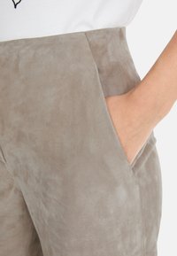 Graue Wildlederhose mit glatter Textur, hoher Taille und seitlichen Taschen, die ein sauberes Design mit minimalem Nähte aufweist.