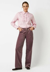 Light pink ruffled button-up shirt with long sleeves, paired with wide-leg, mauve corduroy pants. Textured fabric and structured design.