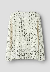 Długi rękaw, kremowy top w czarne groszki, z okrągłym dekoltem i teksturowanym, prążkowanym materiałem. Wzory równomiernie rozmieszczone.