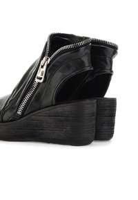 Czarne skórzane botki na koturnie sięgające kostki z bocznym zamkiem błyskawicznym i otwartym tyłem. Teksturowana pięta z rowkami dla lepszej przyczepności.
