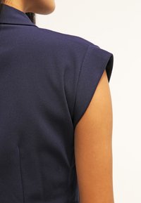 Mörkblå, kortärmad topp med en slät tygstruktur, med en figursydd design och rundad axelsnitt som exponerar en del av armen.