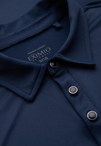 Polo shirt blu navy con una texture liscia, dotato di colletto classico e tre bottoni. L'etichetta riporta "EXIMIO" con "QUALITÀ PREMIUM."