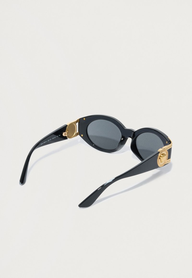 Schwarze Sonnenbrille mit ovalen Gläsern, goldenen Akzenten an den Bügeln und strukturierten Hardware-Details. Glänzende Oberfläche mit einem eleganten Design.