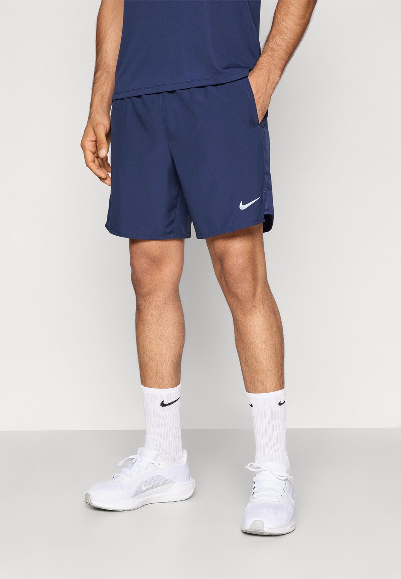 Σκούρο μπλε σορτς Nike με ελαστική μέση, πλαϊνές τσέπες και λευκό λογότυπο swoosh. Συνδυασμένα με λευκά αθλητικά παπούτσια και κάλτσες.