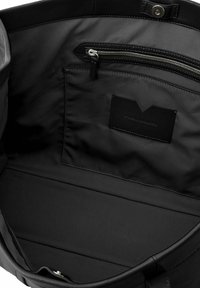 Interno di una borsa in pelle nera con texture liscia, una tasca con zip e un portacarte. Il dettaglio della cucitura è sottile e coerente in tutto il progetto.