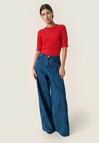 Rød, ribbet top med korte ærmer, parret med højtaljede, vide blå denimjeans. Stoffet ser glat ud med synlige sømme og lommer.