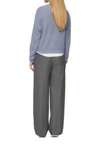 Hellblauer, gestrickter Pullover mit lockerer Passform und Raglanärmeln, kombiniert mit grauen, taillierten, weit geschnittenen Hosen und einem weißen Unterhemd.