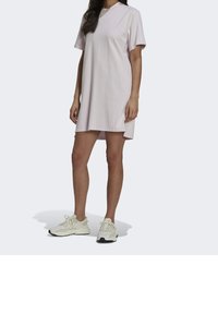 Różowa sukienka z bawełnianej dzianiny, z krótkimi rękawami i okrągłym dekoltem, z prostym dołem i minimalistycznym logo. Noszona z białymi trampkami.