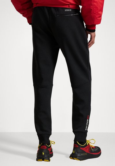 Pantalons de jogging noirs en tissu doux, avec une coupe slim et des poignets élastiques. Détails notables : une poche arrière avec une fermeture éclair élégante.