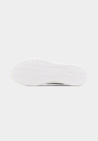 Λευκό πέλμα αθλητικού παπουτσιού με μοτίβο πλέγματος και το λογότυπο "Calvin Klein" στο κέντρο, εμφανίζεται πάνω σε ένα απλό ανοιχτόχρωμο φόντο.