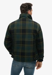 Karierte Jacke in dunklem Grün, Schwarz und Gelbtönen, mit hohem Kragen und geknöpften Manschetten. Strukturierter Stoff mit klassischem Karomuster.