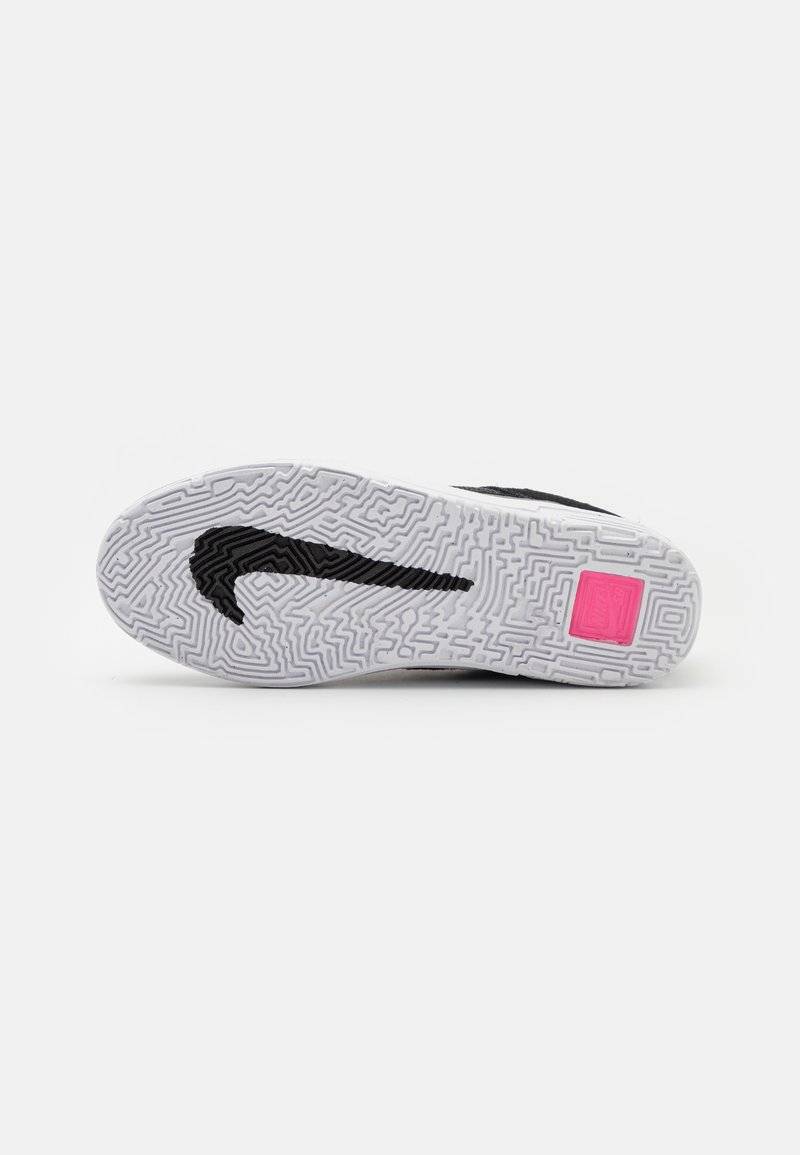 Suela de zapatilla deportiva en blanco y negro con goma texturizada, que presenta un prominente logo de swoosh de Nike en negro y un bloque de acento en rosa.