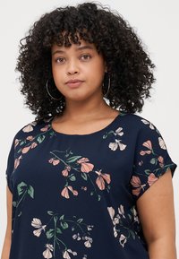 Navy blue top with short sleeves, featuring a floral pattern in pink and green hues. Soft fabric with a scoop neckline and relaxed fit.
