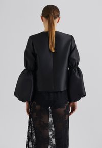 Svart satengbluse med voluminøse, rynkete ermer og åpning bak. Sammen med et lagdelt svart blonde skjørt med blomstermønster.