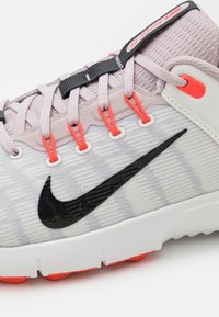 Nike kurpes ar gaiši pelēku sieta augšdaļu, melnu swoosh, oranžiem akcentiem un baltu zoli ar sarkaniem zoles elementiem.