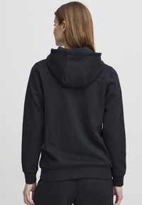 Svart hettegenser med snøring, teksturert stoff og ribbede mansjetter, med et enkelt design uten synlige logoer eller mønstre.