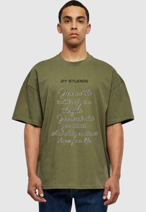 Olivgrünes Baumwoll-T-Shirt mit oversized Passform, Rundhalsausschnitt und kurzen Ärmeln. Die Vorderseite zeigt weißen Text mit einem motivierenden Zitat und dem Markennamen.