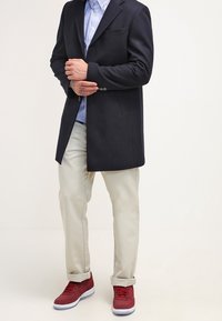 Marinblå ullblandat riktning med urklippta slag, över en ljusblå skjorta, parat med uppvikta beige byxor och röda sneakers.