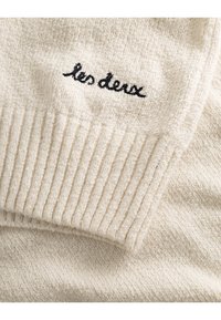 Krämfärgad tröja med ribbade manschetter. Har ett mjukt, texturerat tyg och en svart broderad "les deux"-logotyp fram.