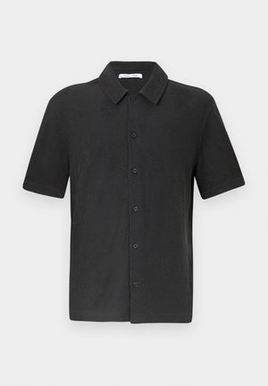 Camisa negra de manga corta con cuello abotonado, que presenta un sutil patrón texturizado y cierre frontal de botones. Material de tela suave.
