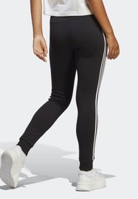 Svarta träningsleggings med tre vita sidstreck, en åtsittande design och ankle cuffs. Bärs med vita sneakers.