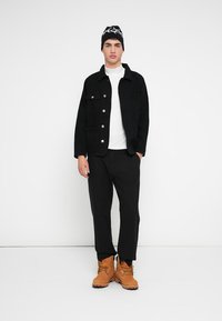 Fekete farmerdzseki ezüst gombokkal, fehér garbó, fekete nadrág és barna bakancsok. Fekete sapka fehér felirattal is szerepel a szettben.