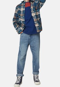 Flannelskjorte i blå, brun og hvid tern, marineblå T-shirt, lyseblå jeans og marineblå sneakers med hvide såler og snørebånd.