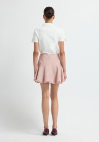 Witte top met korte mouwen en knoopaccenten, gecombineerd met een roze uitlopende rok met een textuurpatroon en een franjerand. Paarse schoenen.