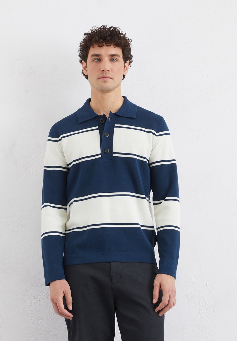 Marineblå og kremfarget stripete langermet polo skjorte med tre svarte knapper. Har en klassisk krage og ribbede mansjetter.