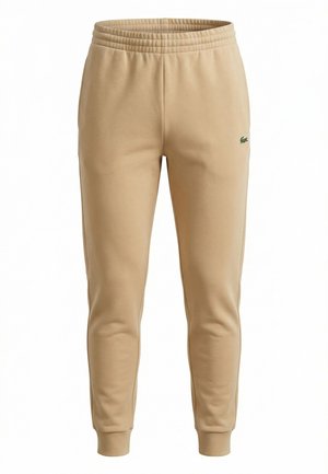 Pantalones jogger beige de corte ajustado con cintura elástica, tobillos ribeteados, bolsillos laterales y un pequeño logo verde bordado en el muslo izquierdo.