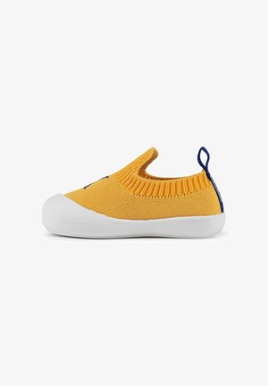 Zapato tipo slip-on de punto amarillo con suela de goma blanca, que cuenta con un cuello acanalado y detalles en azul marino en la parte trasera, diseñado para la comodidad y facilidad de uso.