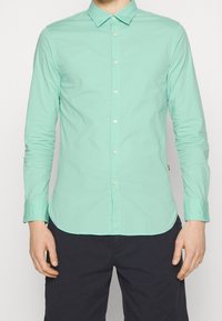 Camicia verde menta a maniche lunghe con colletto button-down, caratterizzata da un design slim fit, bottoni frontali e maniche con polsini.