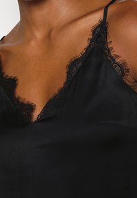 Svart satinspets med en djup V-ringning och intrikata svarta spetkanter längs kanterna samt tunna justerbara axelremmar.