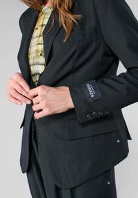 Zwarte gestreepte blazer met notch-lapels en een enkele knopsluiting. Voorzien van een borstzak en vier knoopaccenten op de manchetten.
