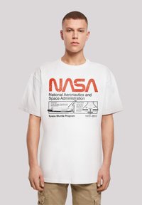 White cotton t-shirt featuring a large red NASA logo and detailed print of the Space Shuttle with program dates, paired with beige cargo pants.