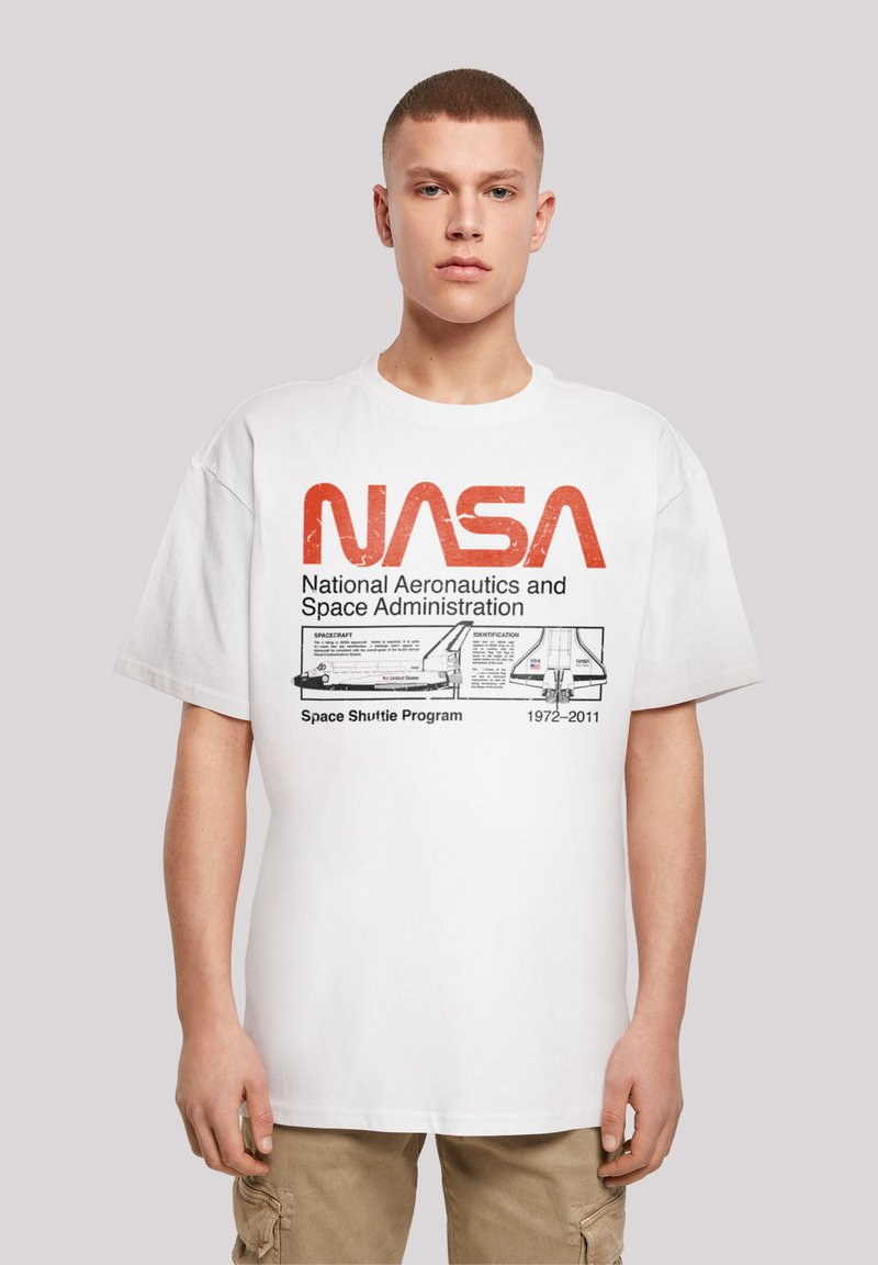 White cotton t-shirt featuring a large red NASA logo and detailed print of the Space Shuttle with program dates, paired with beige cargo pants.