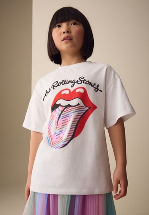 Barn med kort mørkt hår iført en hvid Rolling Stones t-shirt med røde læber og et farverigt stribet tunge-design.