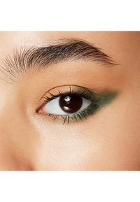 Close-up van een oog met een bruine iris en lange wimpers, met groene eyeliner op het onderste ooglid en een lichtbeige oogschaduw.
