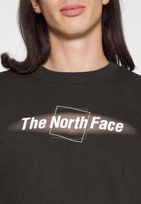 Mörkgrön sweatshirt i bomull med rundad hals. Har vit text "The North Face" med en intilliggande geometrisk grafik.