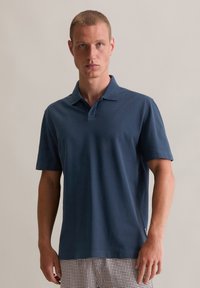 Marineblauwe polo gemaakt van zachte katoen met een klassieke kraag, korte mouwen en een rechte zoom, aangevuld met subtiele zijsplitten.