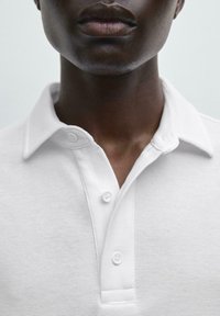 Bílé polo tričko s texturovaným tkaním, klasickým límcem a třemi knoflíky. Hladká tkanina s čistým, minimalistickým designem.