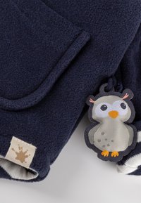 Marineblaues Fleece-Gewebe mit einer Eulenform-Applikation in Orange, grauen Details und einem Etikett mit einem braunen Spritzdesign.