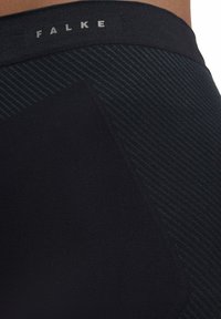 Leggings noirs avec un motif texturé, dotés d'une taille lisse avec le logo "FALKE". Le matériau semble extensible et ajusté.