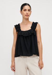 Top nero senza maniche con dettagli arricciati attorno al colletto e alle spalline. Vestibilità ampia, realizzato in tessuto leggero. Abbinato a pantaloni chiari.