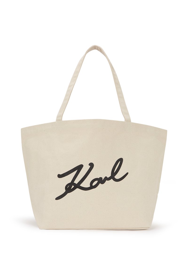 Bolsa de lona en blanco roto con el diseño de firma "Karl" en negro. Cuenta con dos asas resistentes y una silueta amplia y sin tapa.