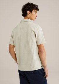 Cămașă cu mâneci scurte, bej deschis, cu un model texturat, guler deschis și slituri laterale; modelul întors, asortată cu pantaloni negri închis.